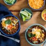 Two bowls of chili with lots of accompaniments