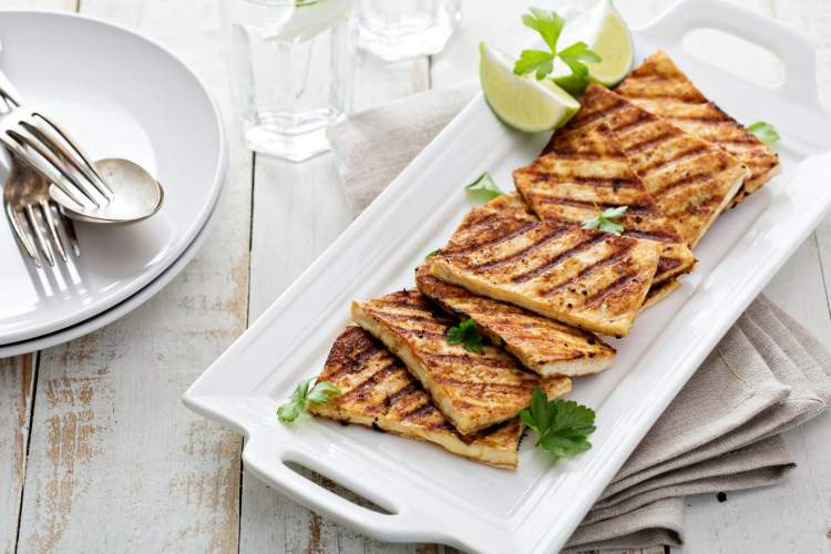 Grilled tofu with cilantro and lime on a white plate with a fork and napkin.